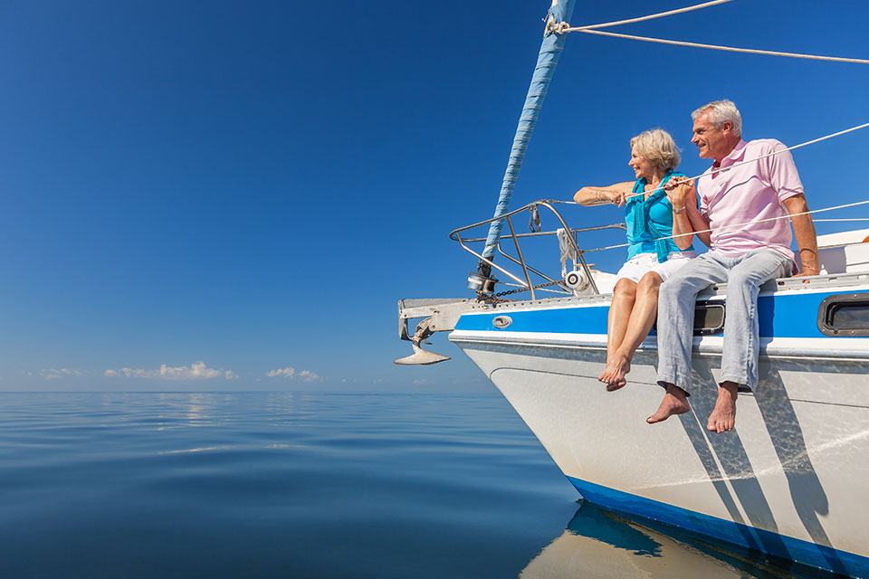 Ein glückliches älteres Paar sitzt auf der Seite eines Segelboots auf einem ruhigen blauen Meer