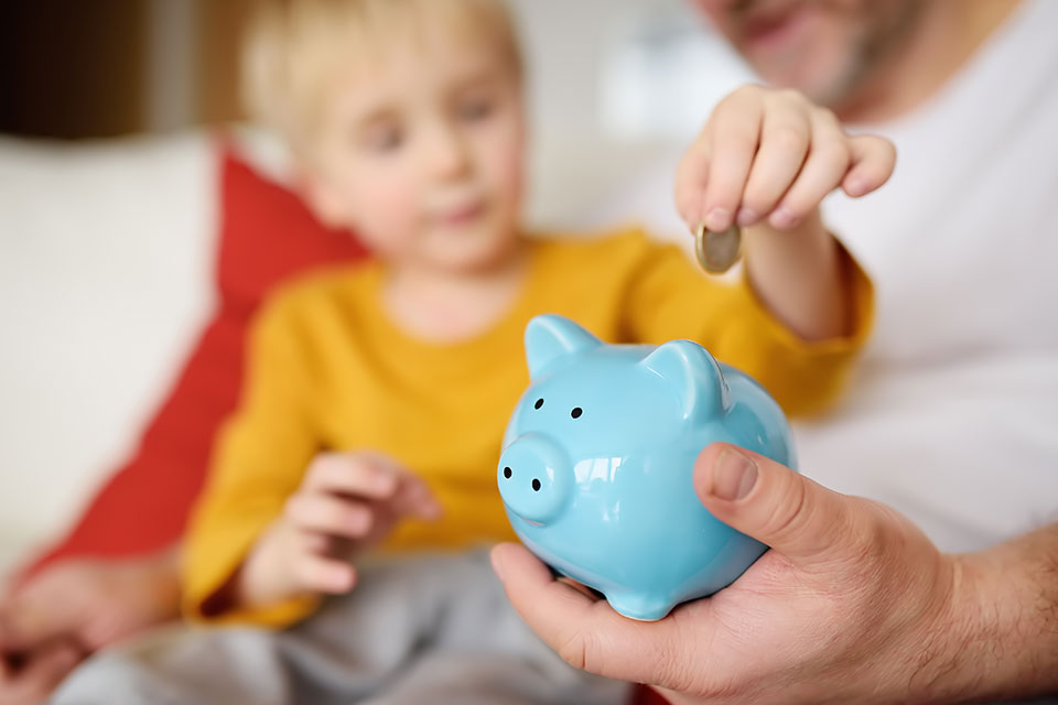 Vater und Sohn werfen Münze ins Sparschwein. Bildung von Kindern in Finanzkompetenz