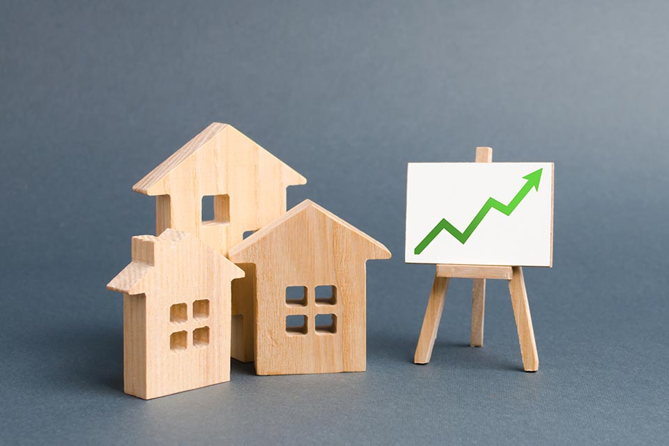 Holzfiguren von Häusern und ein Poster mit grünem Pfeil nach oben. Erhöhen Sie die Liquidität und Attraktivität von Vermögenswerten. Erhöhung der Miete oder der Kosten für den Kauf eines Hauses. Das Konzept der Wertsteigerung von Immobilien.